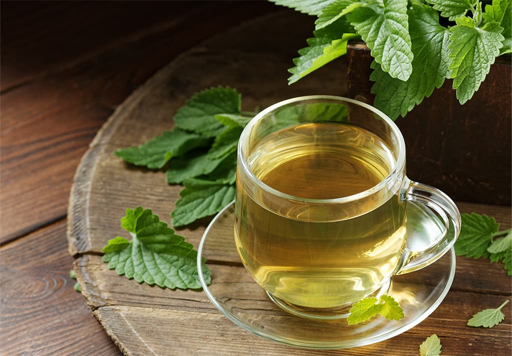 Kräutertee in Glas auf Holztisch mit frischen Minzblättern