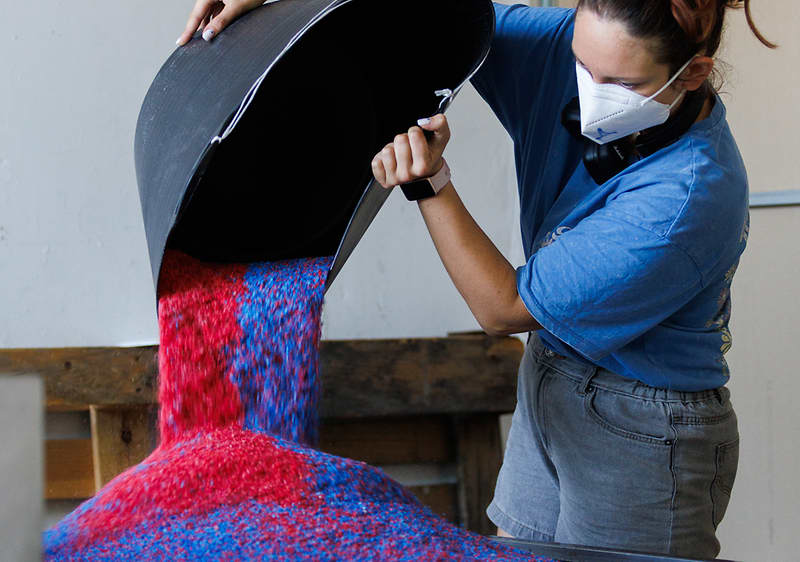  Човек изсипва цветни пластмасови гранули за рециклиране