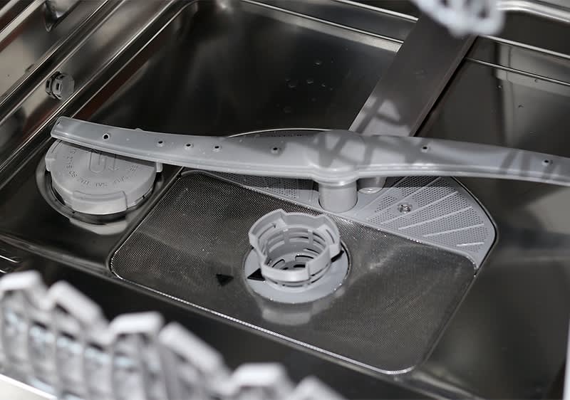 Вътрешността на съдомиялна машина с видими пръскащи рамена и филтър