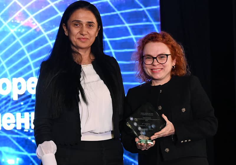 Две жени държат награда на сцена с осветление.