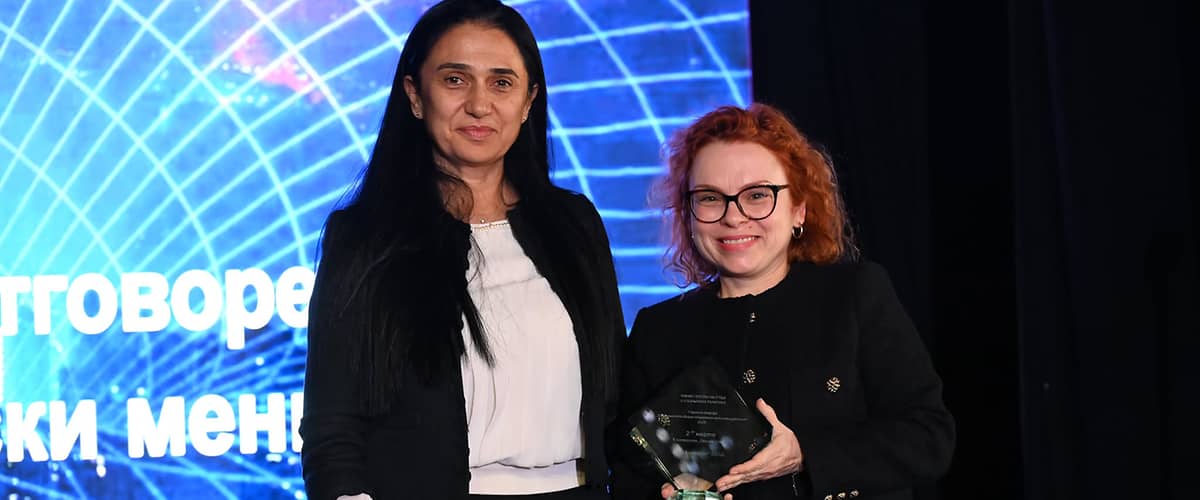 Две жени държат награда на сцена с осветление.