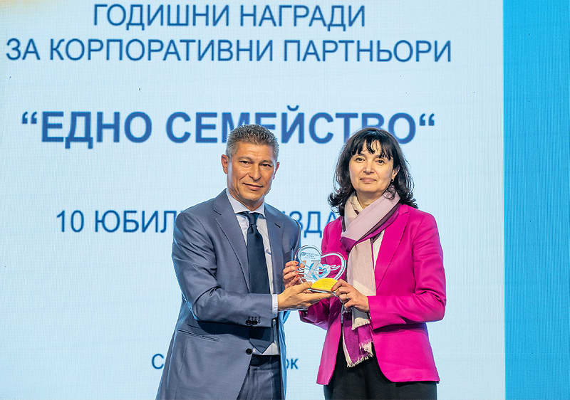 Двама души държат награда пред екран с текст за годишни награди.
