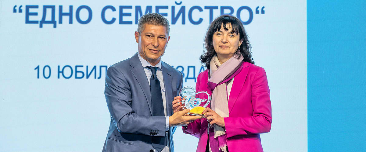 Двама души държат награда пред екран с текст за годишни награди.