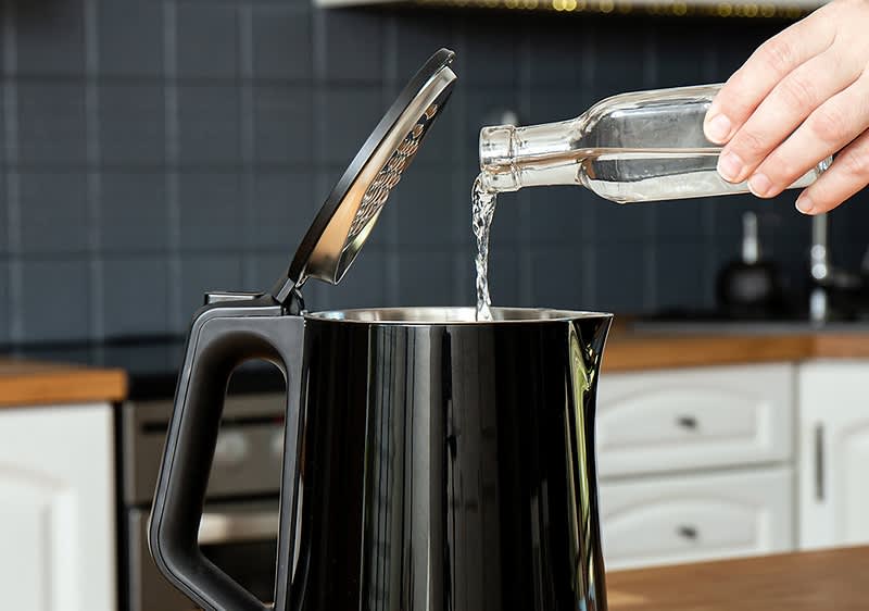 Wasser wird aus einer Glasflasche in einen offenen schwarzen Wasserkocher gegossen