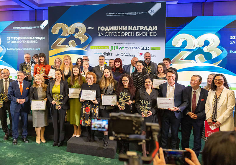 Две жени държат сертификат на събитие с банер на заден план.