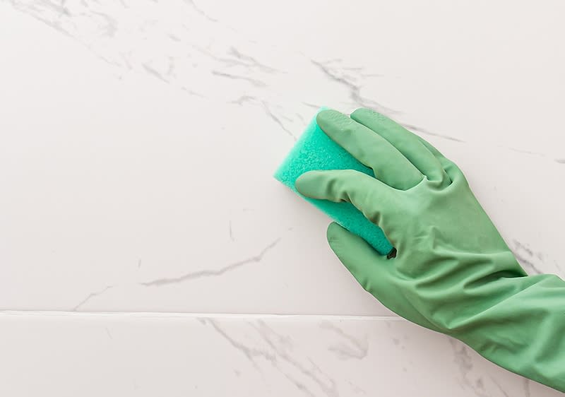 Eine Hand in einem grünen Gummihandschuh reinigt mit einem grünen Schwamm eine weiße Marmoroberfläche
