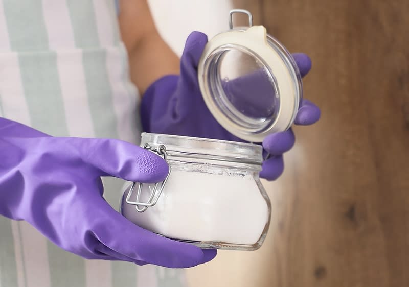 Person in lila Handschuhen hält ein offenes Glas mit weißem Pulver in der Hand