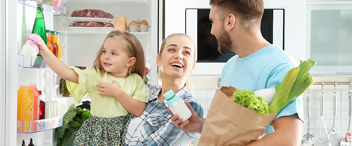 Familie vor Kühlschrank mit Einkauf
