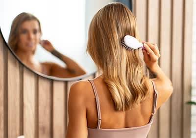 Frau bürstet blondes Haar vor Spiegel