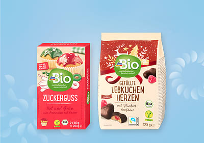 Dva dmBio pakovanja proizvoda: lijevo, crveni i zeleni šećerni posip; desno, punjena srca od medenjaka prelivena čokoladom.