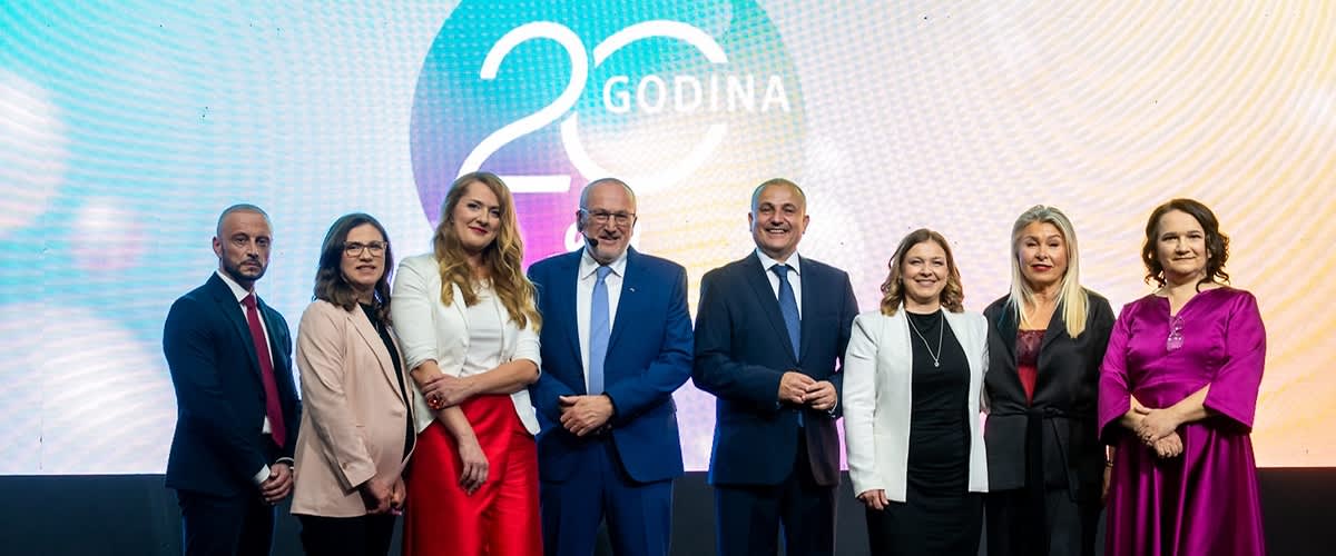 Na slici je grupa ljudi koja pozira ispred šarenog zida s natpisom 20 godina.