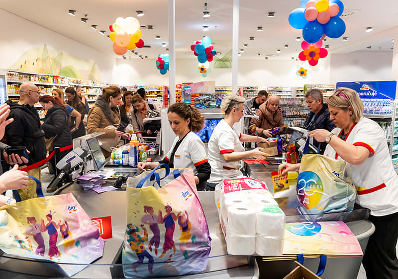 Supermarket s kupcima i blagajnicama, šarene torbe i baloni na pultu