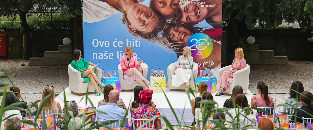 Panel razgovor ispred velikog plakata s nasmijanim ljudima na otvorenom događaju