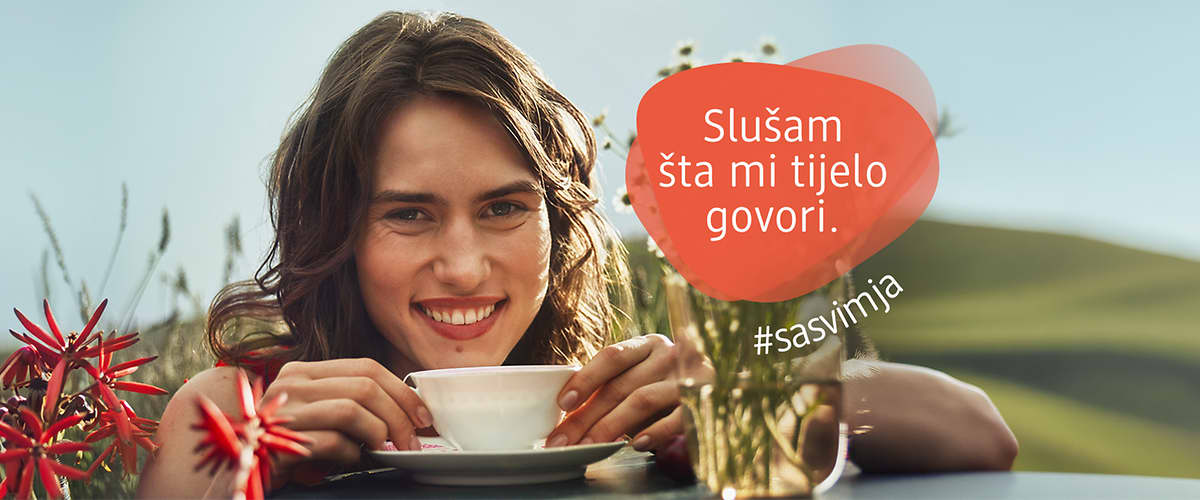 Žena s osmijehom pije čaj u vrtu uz natpis Slušam šta mi tijelo govori