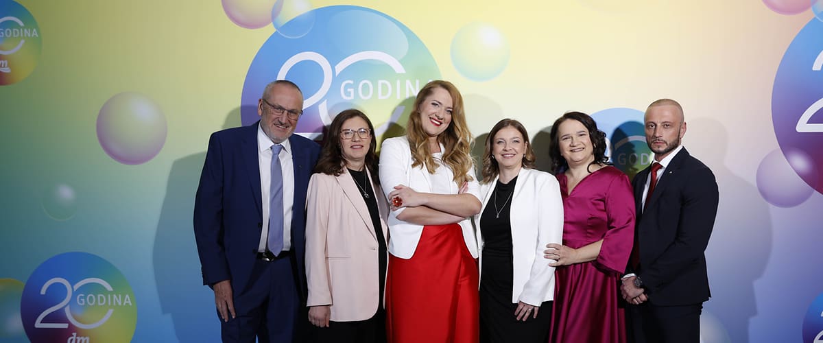 Skupina od šest osoba u svečanim odijelima ispred pozadine s logom 20 godina