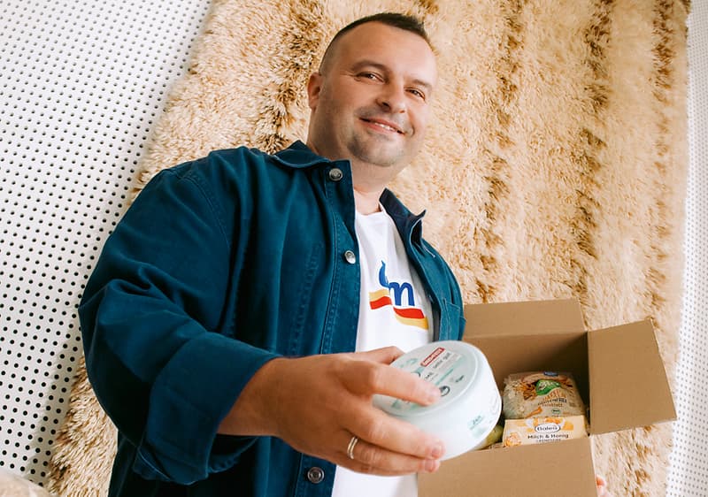 Muškarac drži otvorenu kutiju s prehrambenim proizvodima i posudicu u ruci