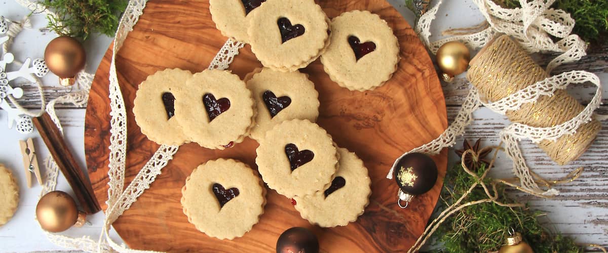 Sušenky s marmeládou na dřevěném prkénku, obklopené vánočními dekoracemi a stuhami