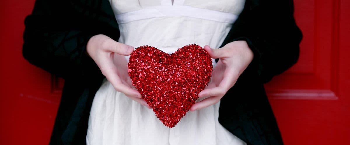 Osoba držící třpytivé červené srdce před bílými šaty