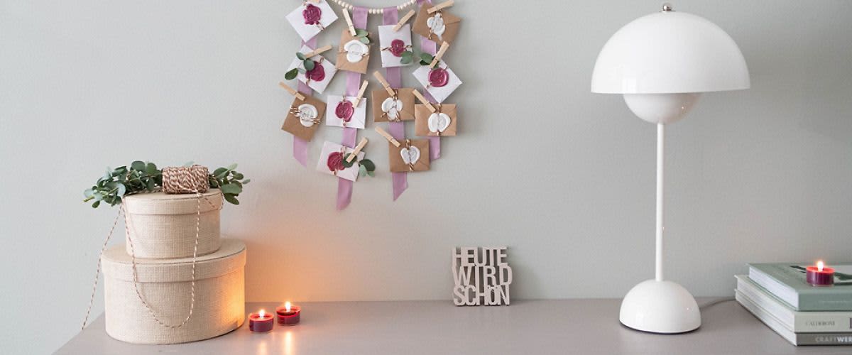 Dekorace na zdi s obálkami, dvě svíčky, dvě krabice a nápis HEUTE WIRD SCHÖN na stole