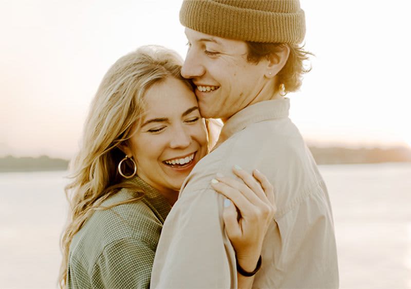 Pár objímající se u vody při západu slunce