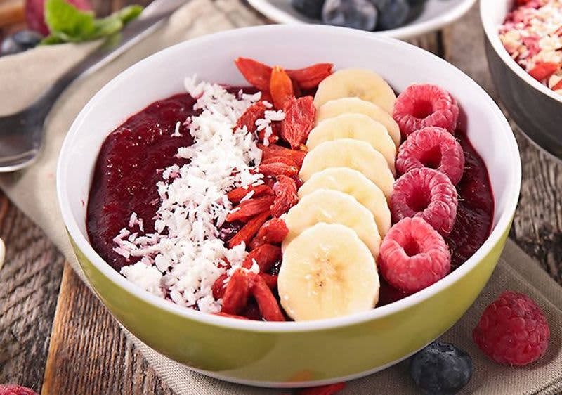Smoothie bowl s banánem, malinami, goji, kokosem a borůvkami na dřevěném stole