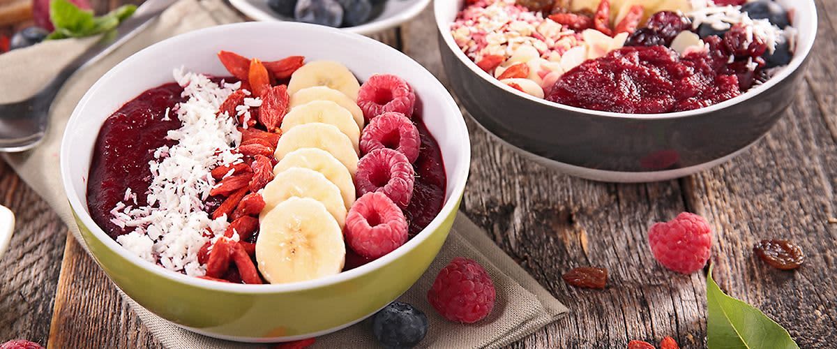 Smoothie bowl s banánem, malinami, goji, kokosem a borůvkami na dřevěném stole