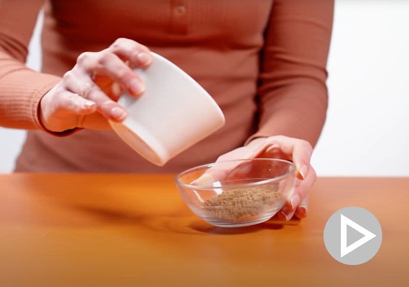 Žena sype koření z bílé misky do skleněné misky na dřevěném stole.