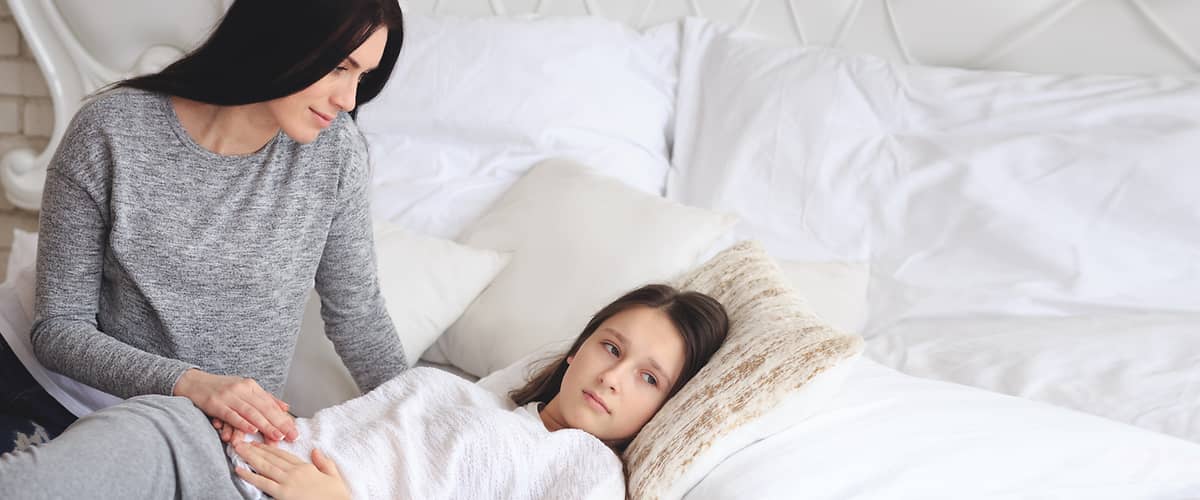 Žena sedící na posteli drží ruku na břiše ležící osoby.