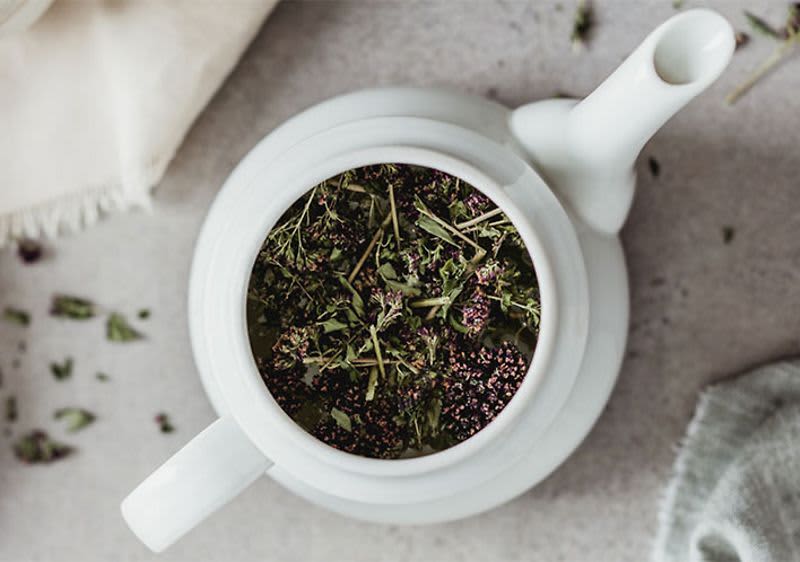 Bílá konvice s čerstvými bylinkami uvnitř na světlém povrchu.