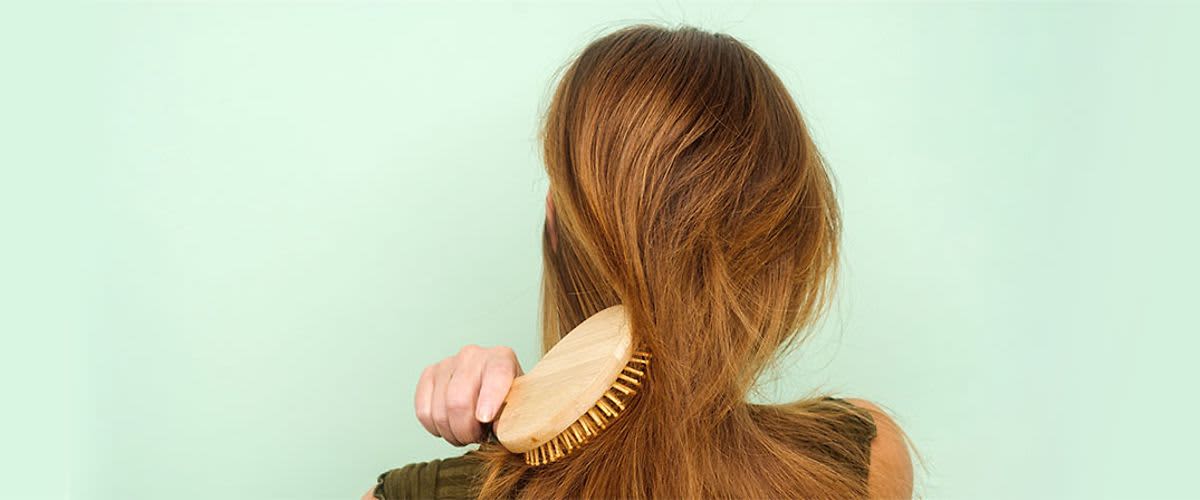 Žena si kartáčuje dlouhé hnědé vlasy na světle zeleném pozadí.