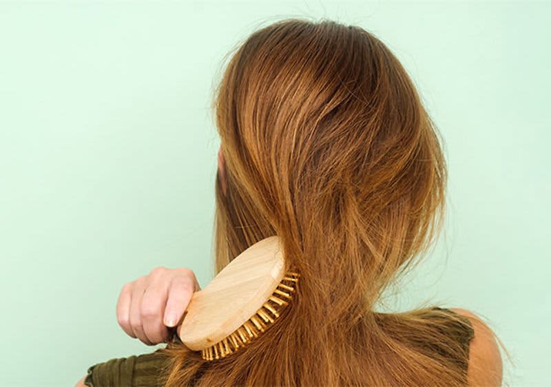 Žena si kartáčuje dlouhé hnědé vlasy na světle zeleném pozadí