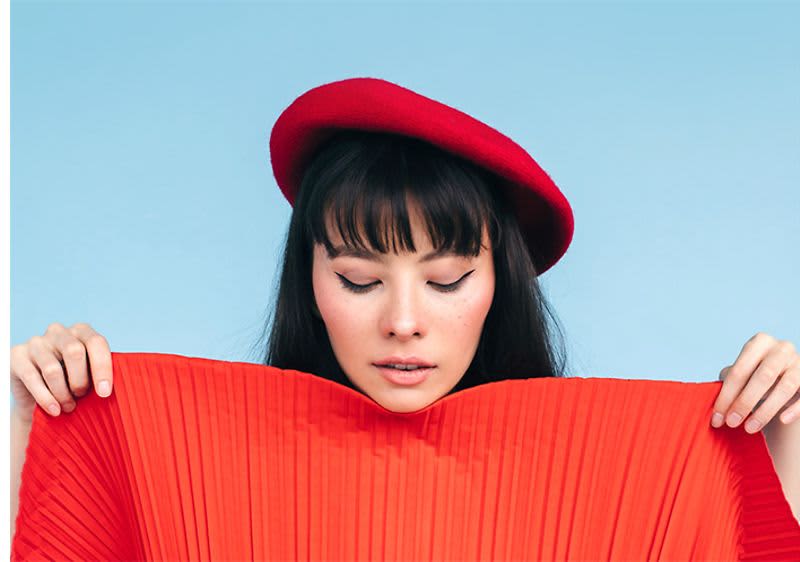 Žena s červeným baretem a červeným plisovaným oděvem