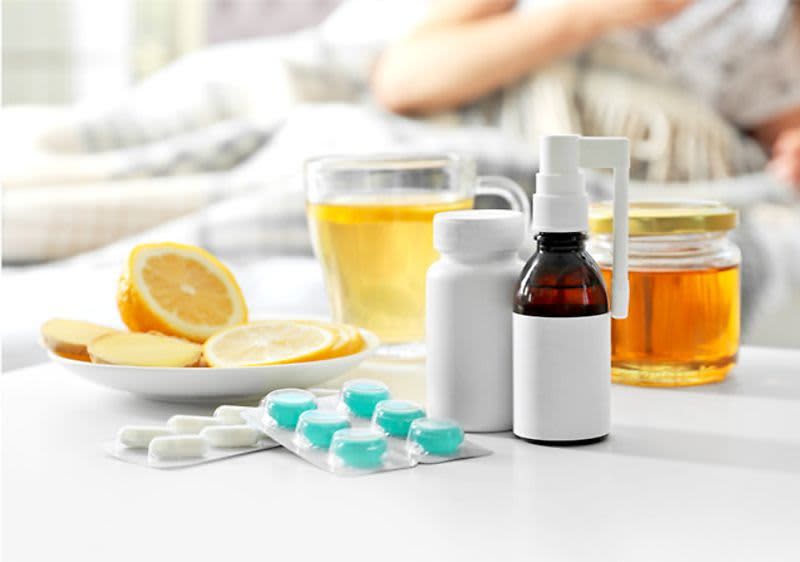 Léky, čaj, citron, med na stole, osoba v pozadí