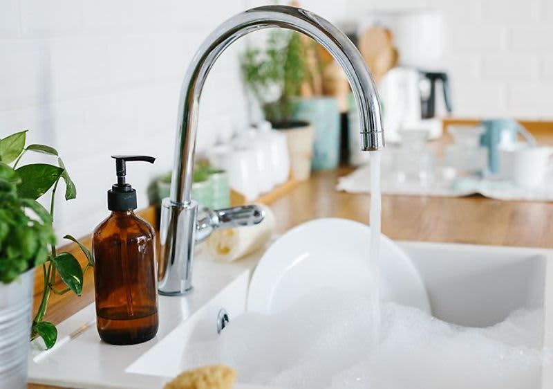 Kuchyňský dřez s tekoucí vodou, mýdlem a nádobím