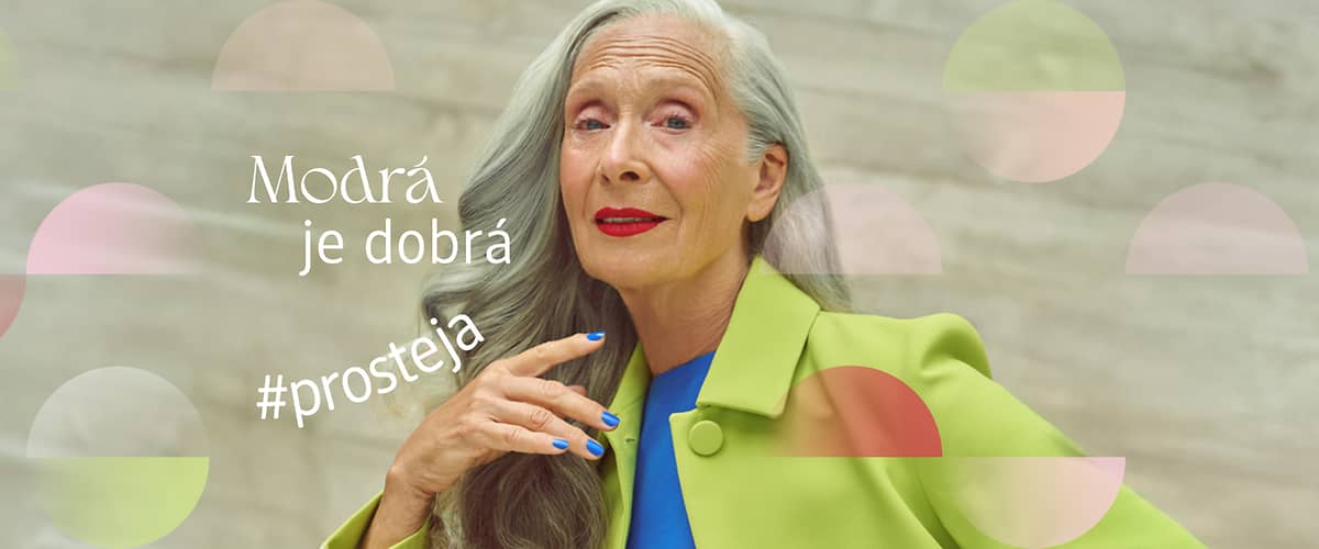 Žena s šedými vlasy v zeleném kabátu, modré nehty, text Modrá je dobrá #prosteja