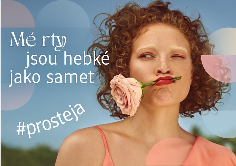 Žena s kudrnatými vlasy a květinou ve vlasech, text Mé rty jsou hebké jako samet a hashtag #prosteja