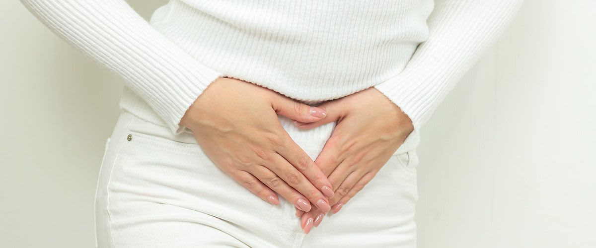 Žena v bílém drží ruce na břiše