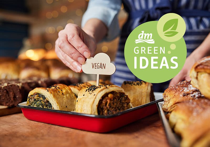 Osoba umisťuje cedulku vegan do pečiva, vedle logo dm GREEN IDEAS