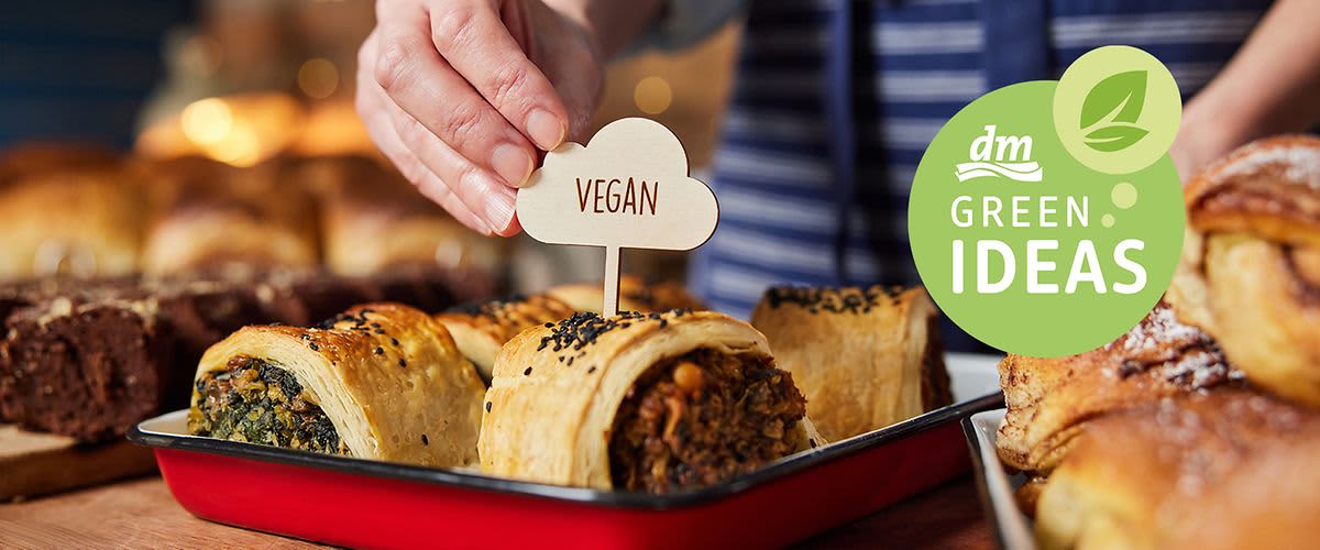 Osoba umisťuje cedulku vegan do pečiva, vedle logo dm GREEN IDEAS