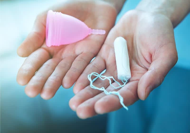 ruce držící menstruační kalíšek a bílý tampon