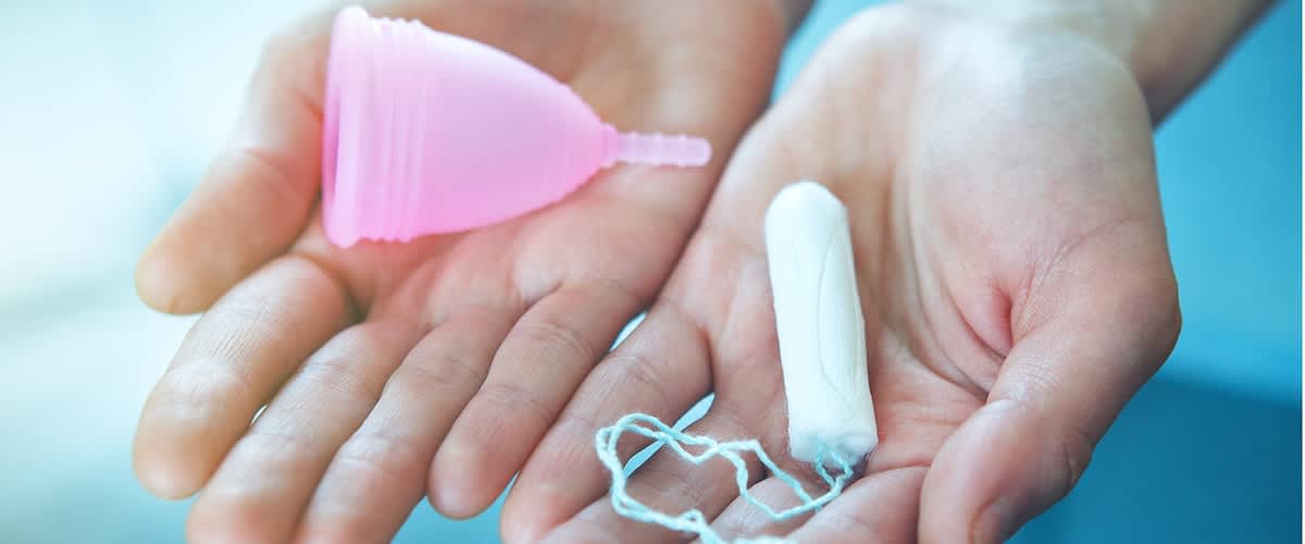 ruce držící menstruační kalíšek a bílý tampon