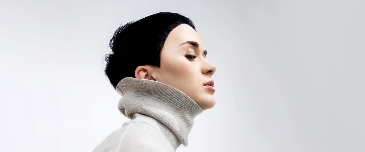 Osoba v šedém roláku s krátkými černými vlasy na neutrálním pozadí