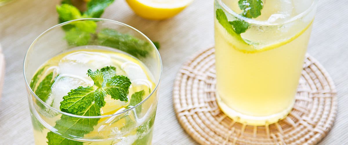 Sklenice citronové limonády s ledem a lístky máty na stole