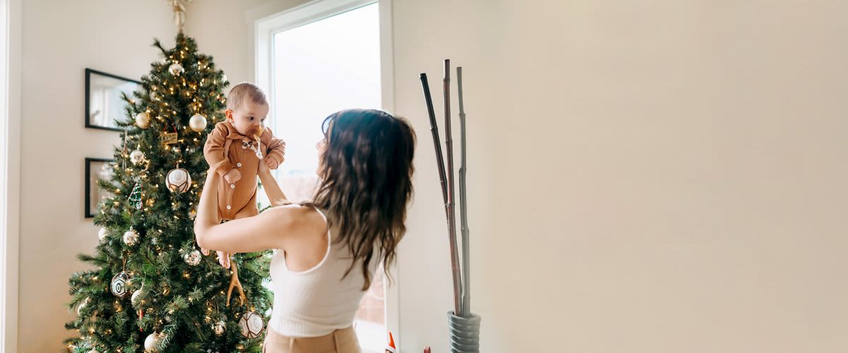 Žena drží dítě před vánočním stromkem v obývacím pokoji.