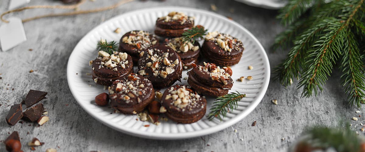 Čokoládové sušenky s oříšky na talíři, vánoční dekorace kolem.