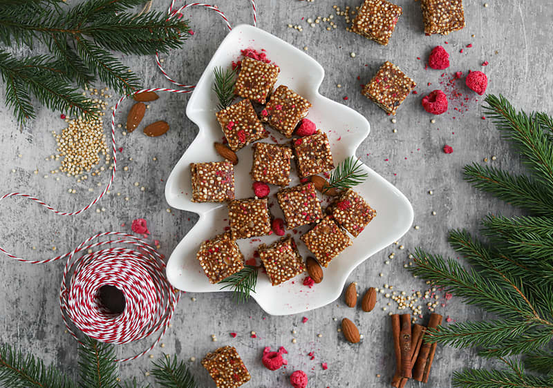 Vánoční talíř s cukrovinkami, mandlemi a malinami, obklopený větvičkami a dekoračním provázkem.