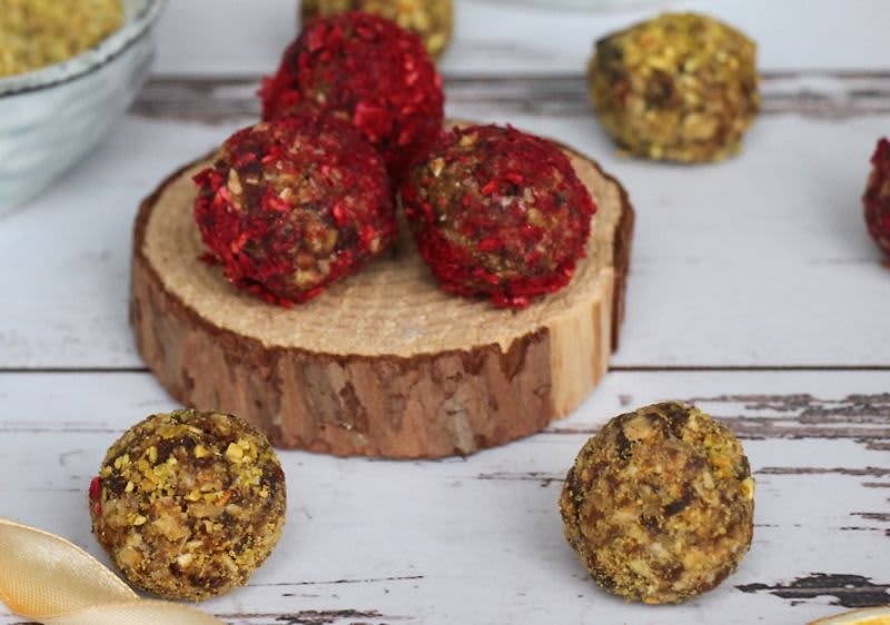 Energetické kuličky na dřevěném podstavci, některé s červeným a jiné se žlutým posypem.