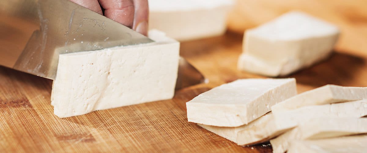 Krájení tofu na dřevěném prkénku kuchyňským nožem