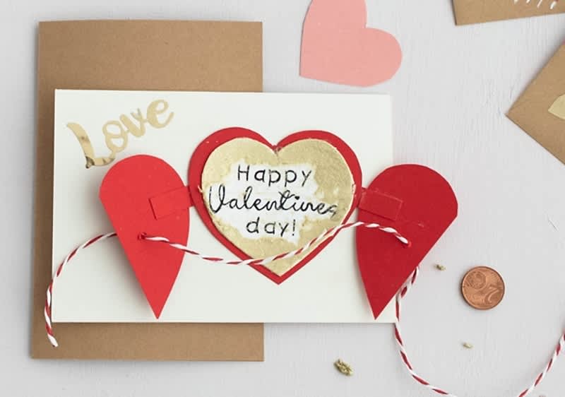 Valentýnské přání s nápisem Happy Valentine's day a červenými srdíčky na bílém a hnědém papíře