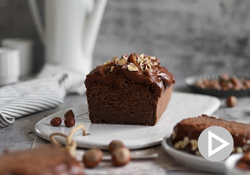 Čokoládový chlebíček s ořechy na talíři, v pozadí konvice a misky s ořechy